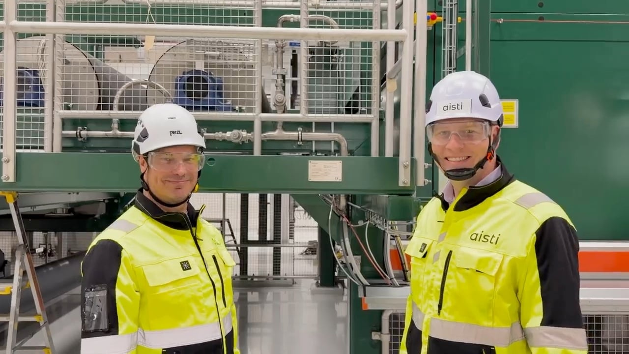 Aistis to stiftere i sikkerhedsudstyr foran den CE-mærkede produktionslinje i Kitee, med CE-pladen på maskinen mellem sig